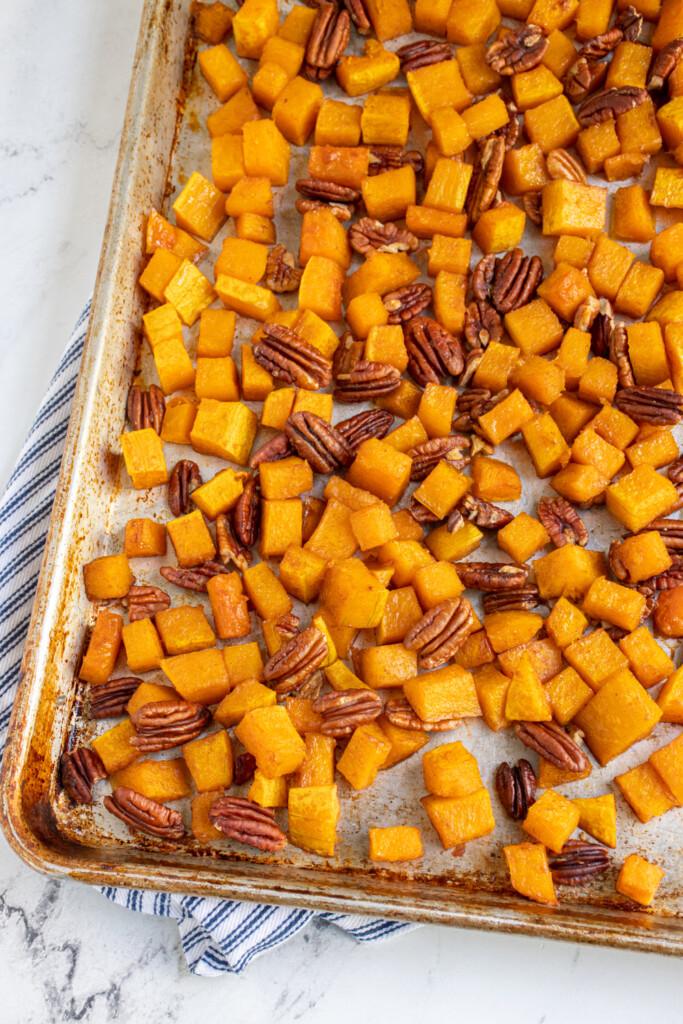 A overhead view of half a sheet pan at an angle filled with cooked butternut squash and pecans.