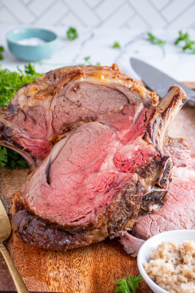 Angle view of a slice of prime rib laid out on a wood cutting board showing the tender juicy insides.