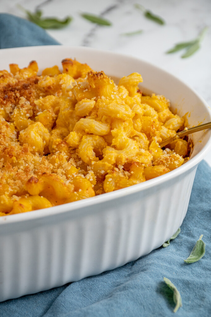 Up close of a white baking dish filled with corkscrew shaped pasta baked pumpkin Mac and cheese with a spoon scooping some out.