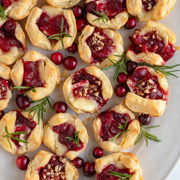 A platter of cranberry brie bites garnished with rosemary and finely diced pecans.