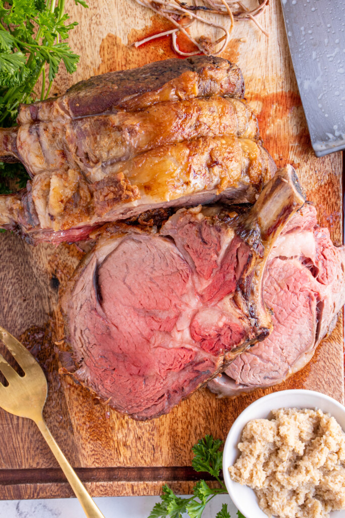 Overhead view of a cutting board with slices of the prime rib next the the roast.