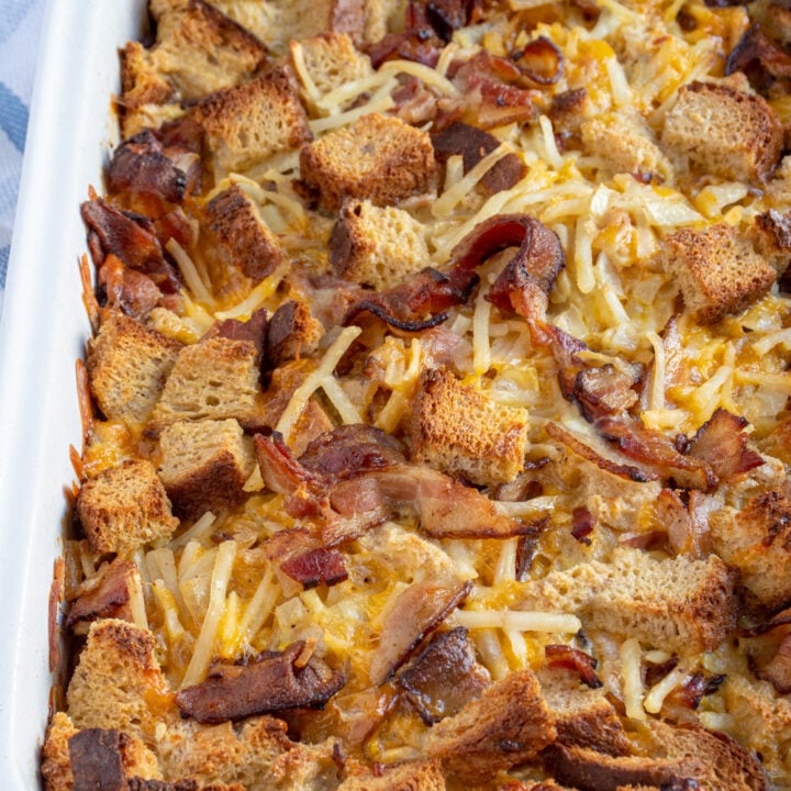 Close up of a dish filled with breakfast casserole with cheese, hash browns, bacon, and bread.
