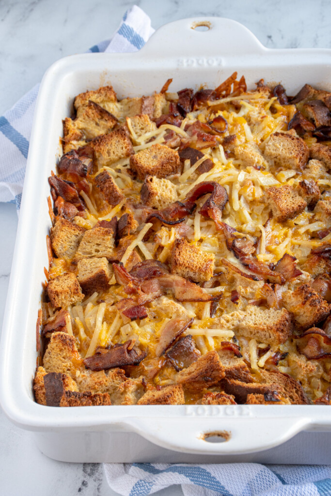 White dish holding baked breakfast casserole with hash browns, bacon, and bread including cheddar cheese.