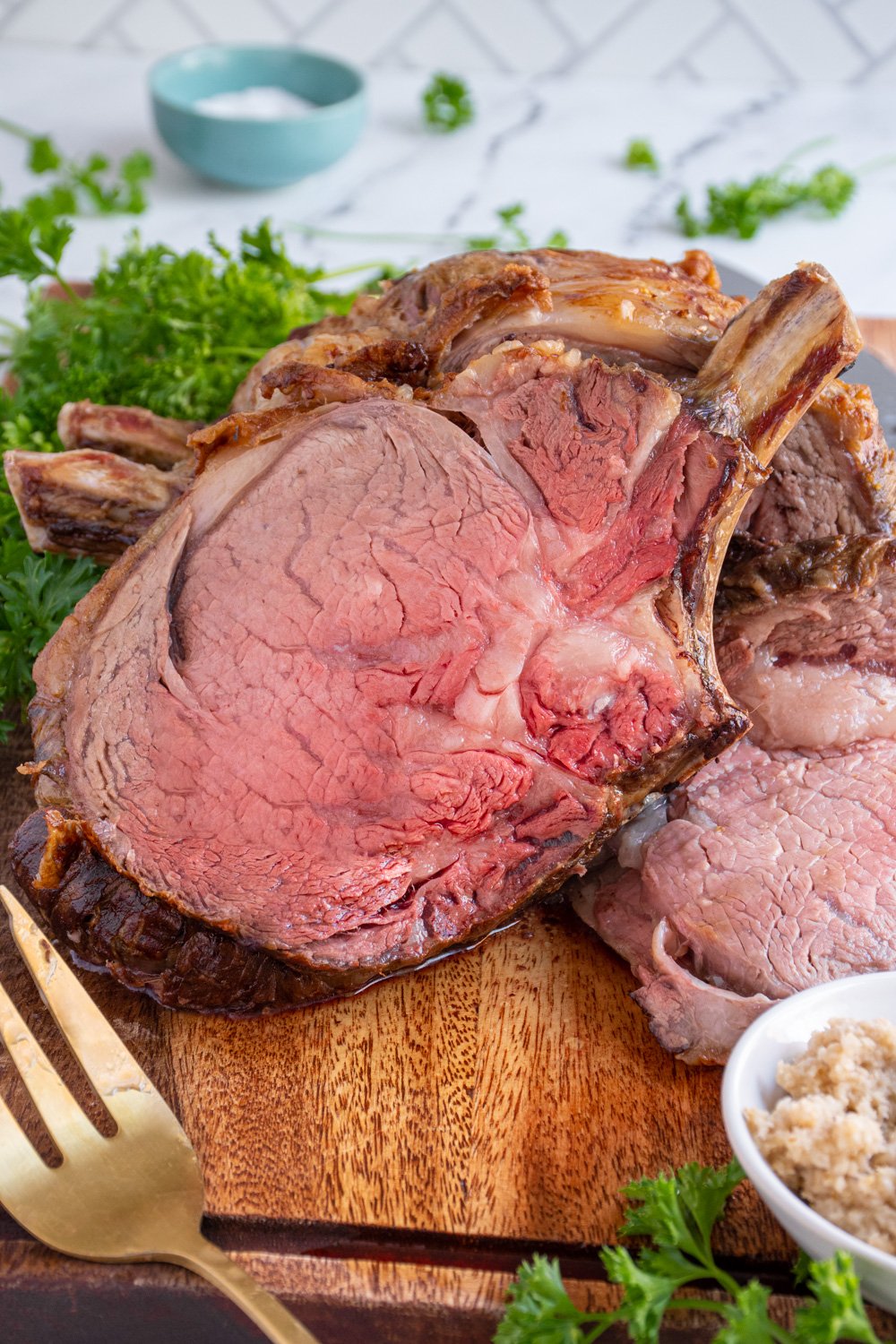 A large slice of prime rib on a cutting board leaned up against the rest of the roast showing off a red tender inside.
