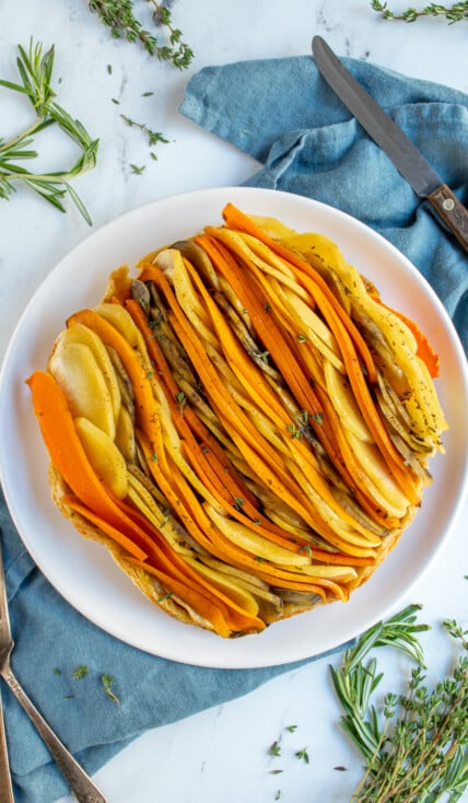 Overhead view showing a savory root vegetable tarte tatin on a plate garnished with fresh thyme showing off the showing of colorful vegetables.