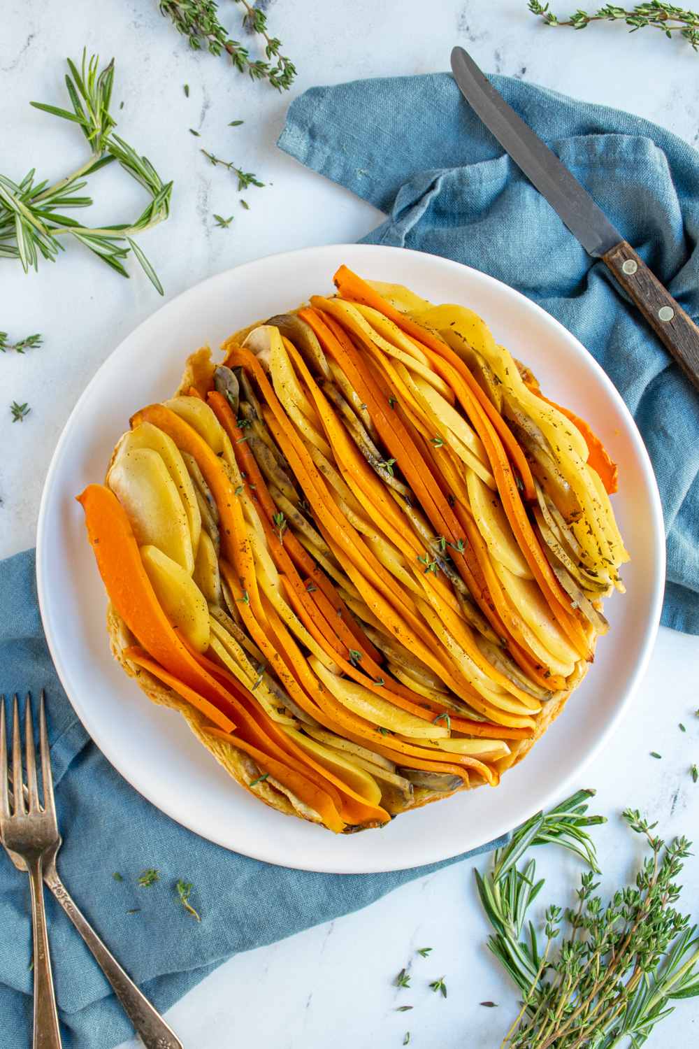 Overhead view showing a savory root vegetable tarte tatin on a plate garnished with fresh thyme showing off the showing of colorful vegetables.