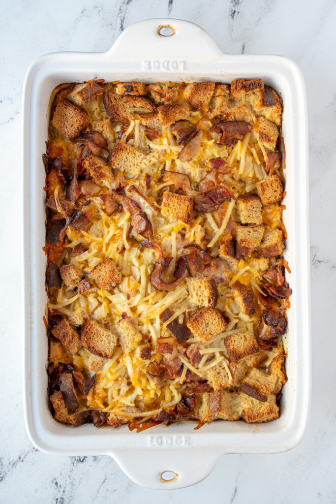 Overhead view of a white dish filled with overnight breakfast casserole with hash browns and bacon.