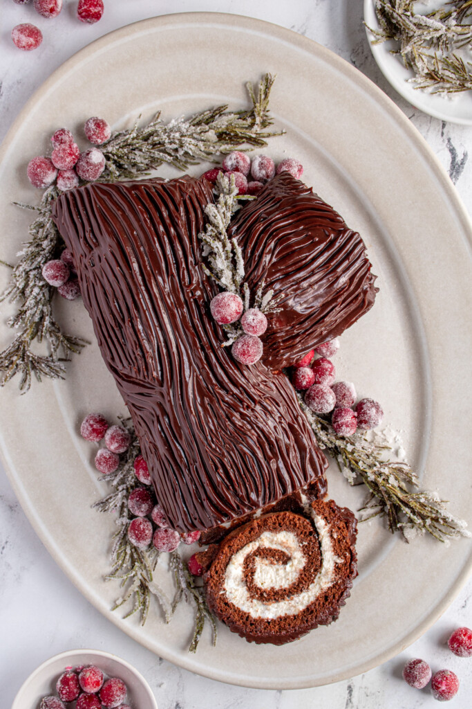 Flatlay of the yule log cake on a platter with a slice off showing the rolled up inside with whipped cream.