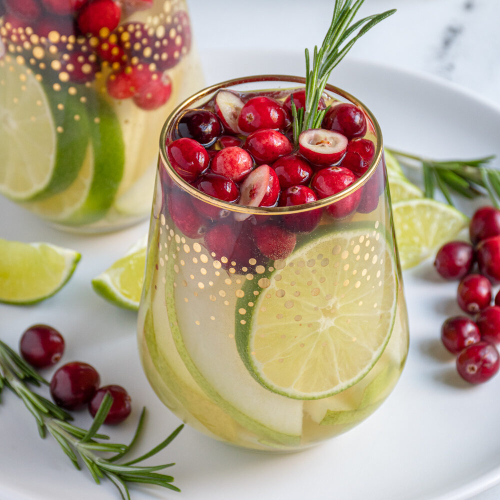 A stemless wine glass filled with White Christmas sangria filled with green pears, limes, and fresh cranberries.