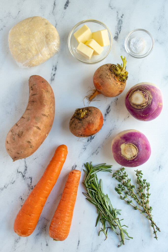 The ingredients needed to make root vegetable tarte tatin laid out on a table top including four different kinds of root vegetables.