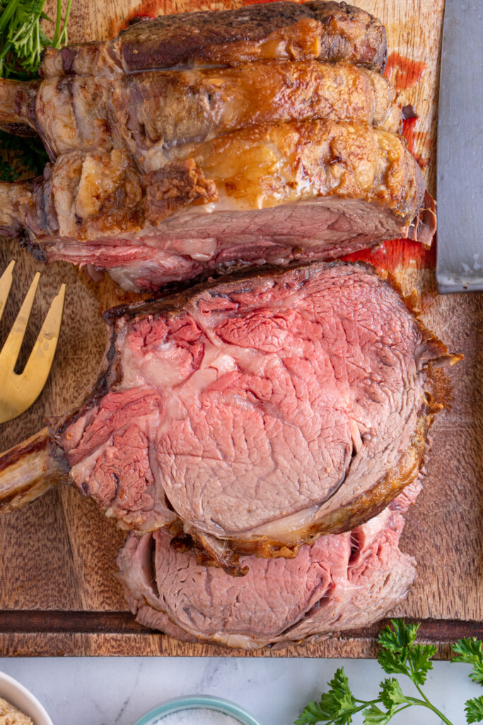 Overhead view of a cutting board with the prime rib being sliced showing off the tender inside.