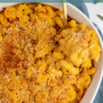 Pinterest pin with text overlay "Baked Pumpkin Mac & Cheese", image of a white casserole dish with a serving spoon scooping out Mac and cheese.