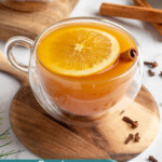 Pinterest Pin with text overlay 'Crockpot Christmas Wassail', image of a crockpot and mugs filled with wassail and garnished with orange slice and spices.