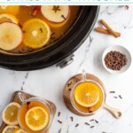 Pinterest Pin with text overlay 'Crockpot Christmas Wassail', image of a crockpot and mugs filled with wassail and garnished with orange slice and spices.