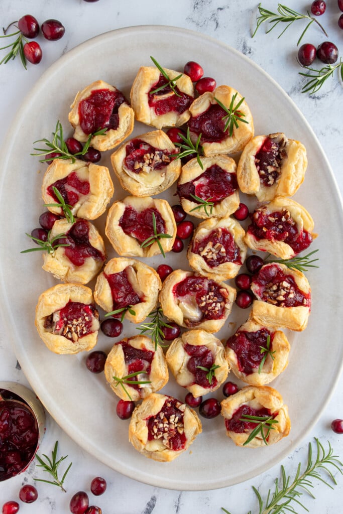 Overhead platter view showing a bunch of cranberry brie bites garnished with rosemary springs and fresh cranberries.