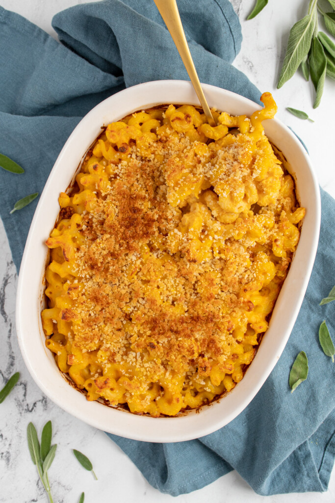 A white casserole dish filled with pumpkin Mac and cheese with a gold serving spoon scooping some out of the corner.