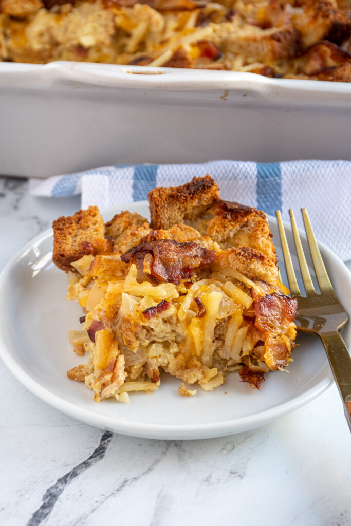 A serving of breakfast casserole with hash browns and bacon on a plate showing off cheese and crispy bread pieces.