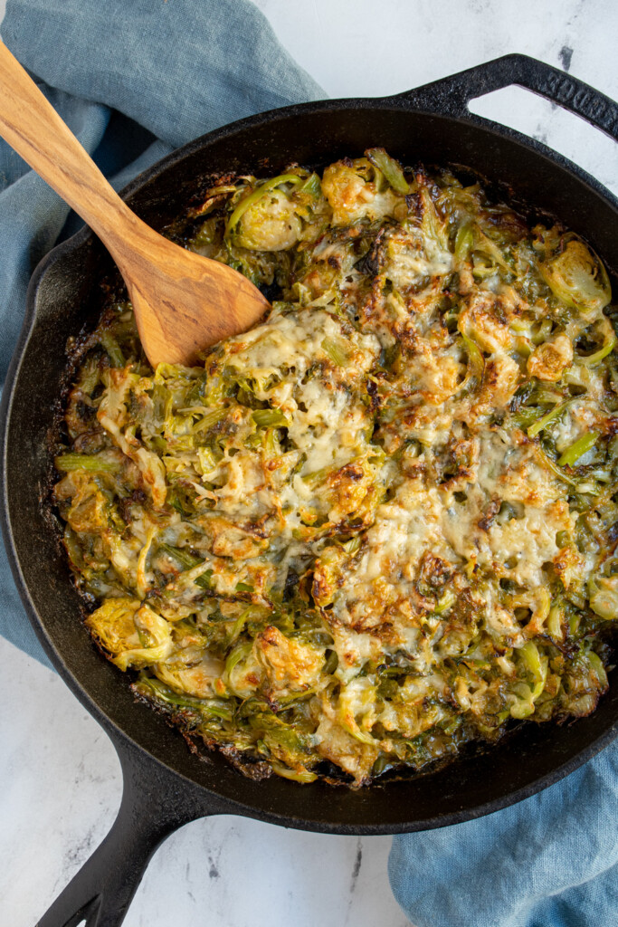 Skillet with a wooden spoon scooping up cheesy brussel sprouts au gratin.