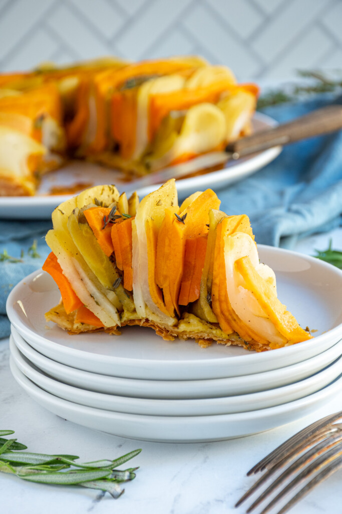 A Slice out of a root vegetable tarte tatin on a plate showing off the vertical rows of colorful veggies baked into a pie.