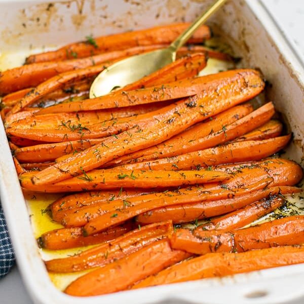 roasted carrots with dill and brown sugar in a white baking dish with a gold spoon