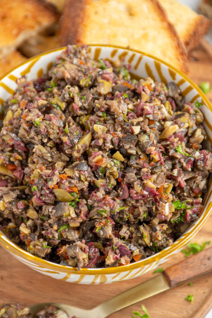 Close up of a white and yellow bowl filled with colorful olive tapenade.