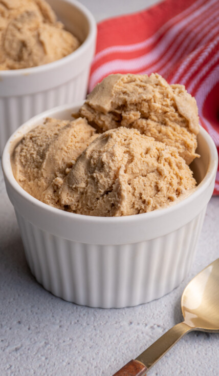 A white bowl filled with scoops of light brown colored gingerbread ice cream sitting next to a spoon.