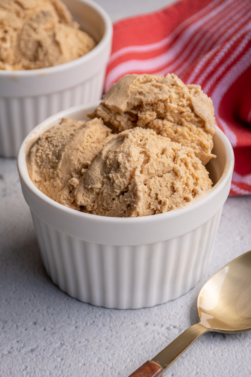 A white bowl filled with scoops of light brown colored gingerbread ice cream sitting next to a spoon.