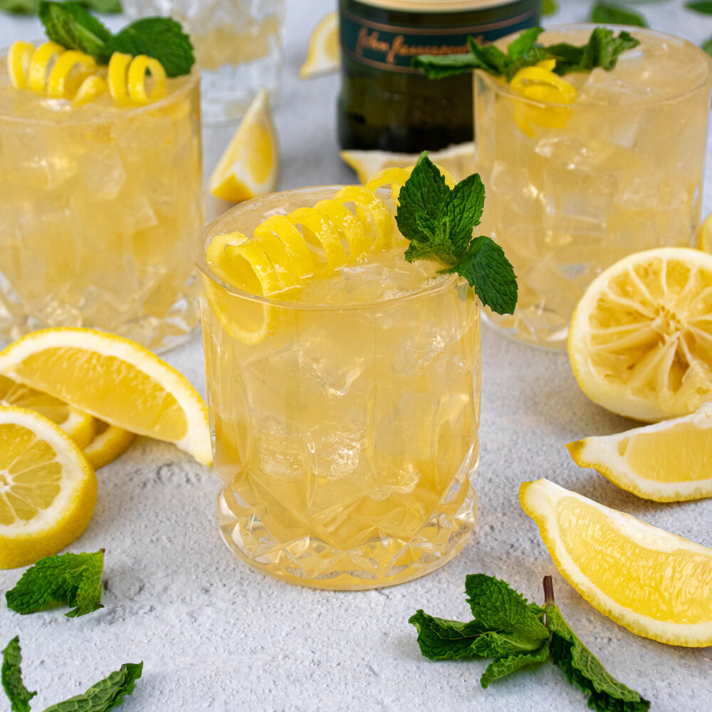 Whiskey glasses on a table filled with ice and Irish Lemonades, garnished with lemon peel and mint leaves.