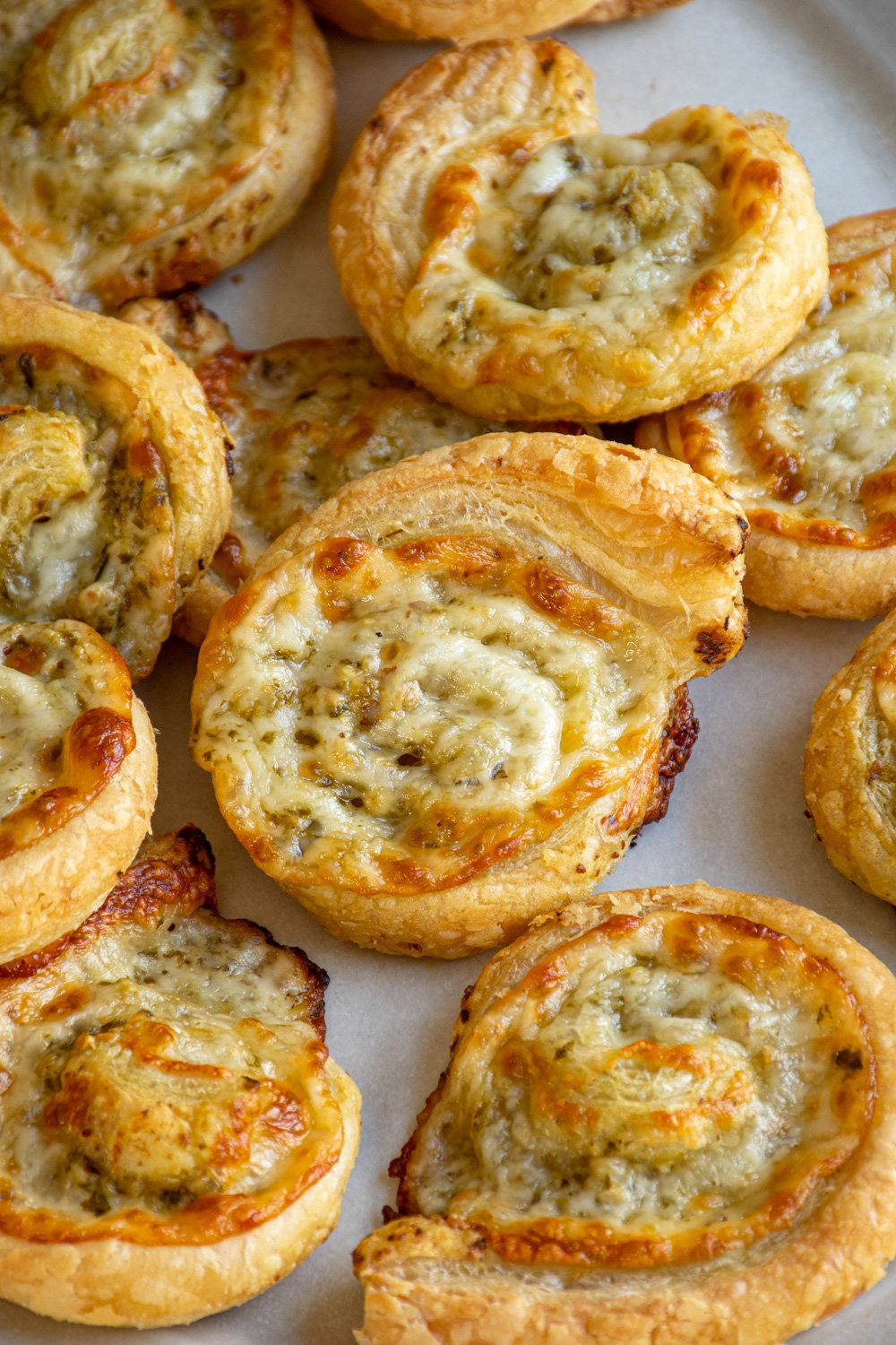 Pesto pinwheels on a platter with the one in the center of focus showing off the melty cheese and pesto center.