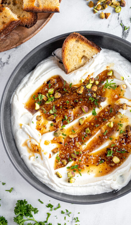 Overhead view of a gray bowl filled with whipped feta dip with honey and garnished with pistachios and parsley.