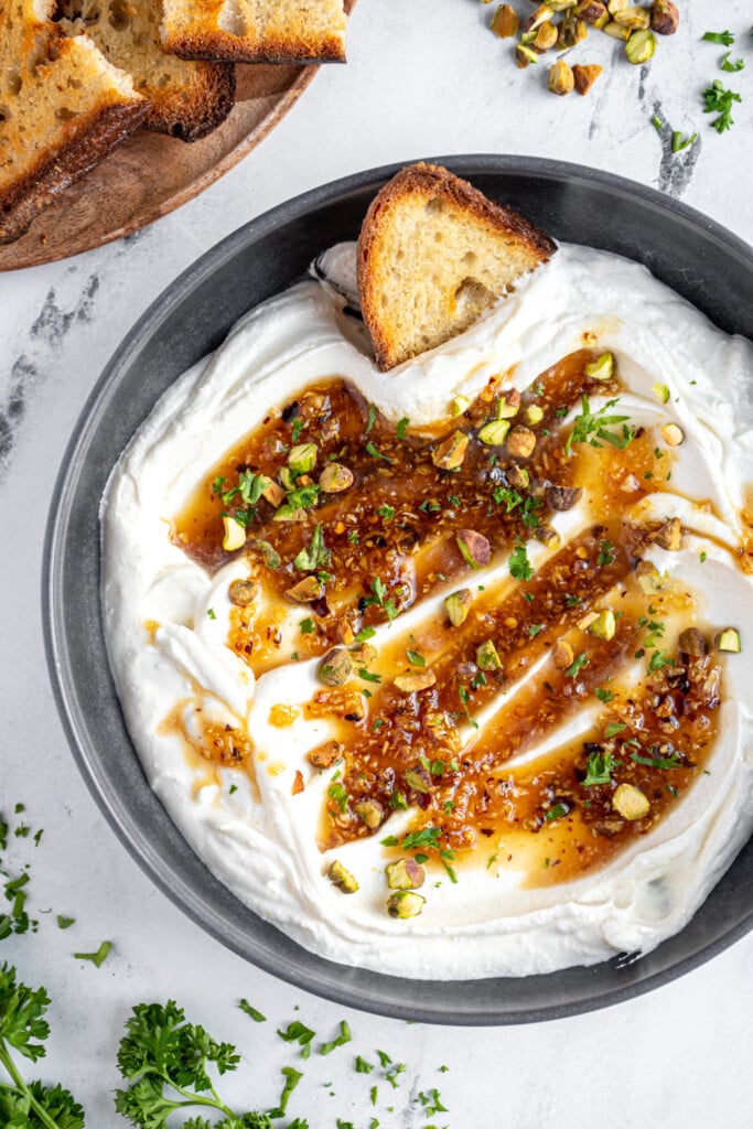 Overhead view of a gray bowl filled with whipped feta dip with honey and garnished with pistachios and parsley.