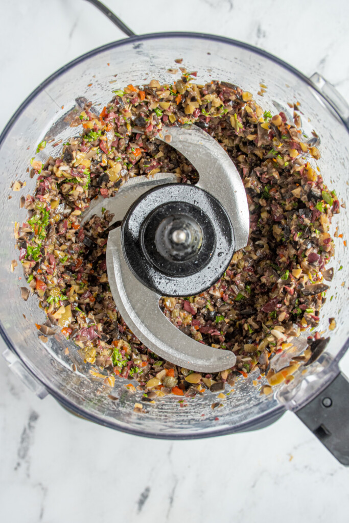 A food processor open with freshly processed olive tapenade.