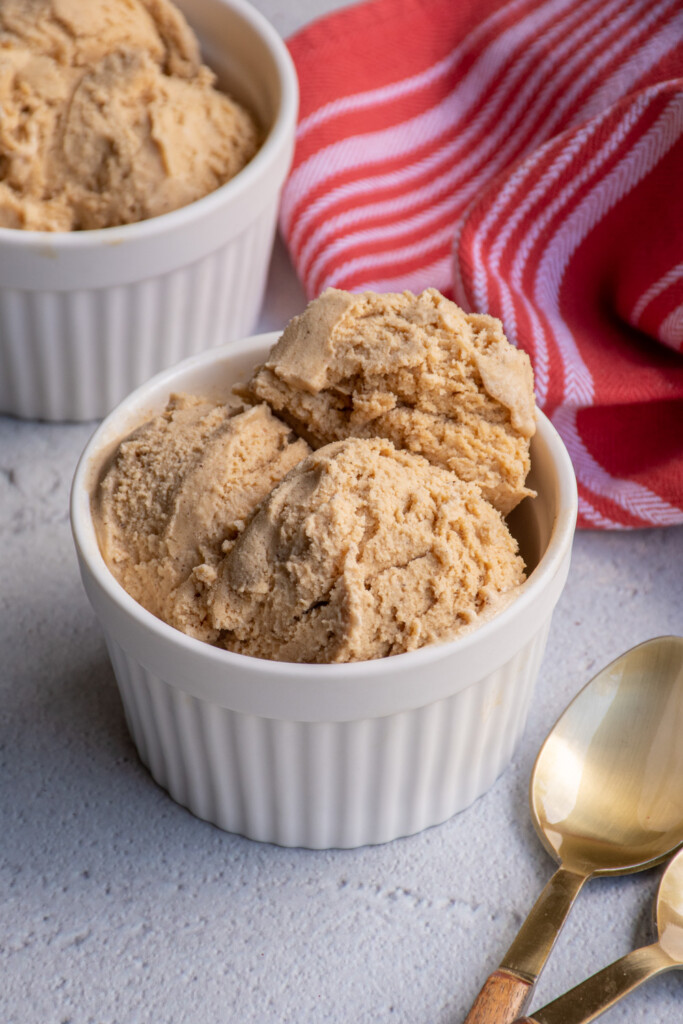 A white bowl filled with gingerbread ice cream next to a pair of gold spoons.