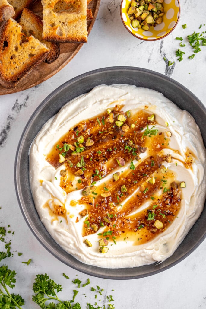 Overhead view of a gray bowl filled with whipped feta cheese and topped with honey and garnished with pistachios and parsley.