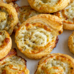 Pinterest pin with logo 'The Schmidty Wife', image of a pesto puff pastry pinwheel on a platter.
