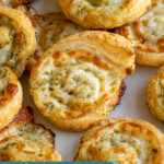 Pinterest pin with text 'Cheesy Pesto Pinwheels', image of a pesto puff pastry pinwheel on a platter.