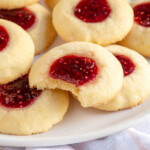 Pinterest pin with logo "The Schmidty Wife", image of a plate of raspberry thumbprint cookies, the center one has a bite taken out.