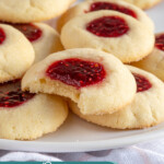 Pinterest pin with text overlay 'Raspberry Thumbprint Cookies', image of a plate of raspberry thumbprint cookies, the center one has a bite taken out.