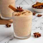 Pinterest pin with logo "The Schmidty Wife", image of a glass filled with a light brown banana chai smoothie with garnishes.