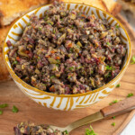 Pinterest pin with logo 'The Schmidty Wife', image of small yellow and white bowl filled with freshly made olive tapenade.