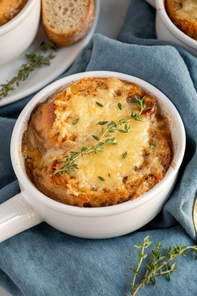 A white bowl filled with slow cooker French onion soup and topped with melted cheese, garnished with fresh thyme.