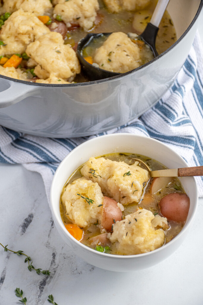 A white bowl filled with veggie soup topped with fluffy dumplings.