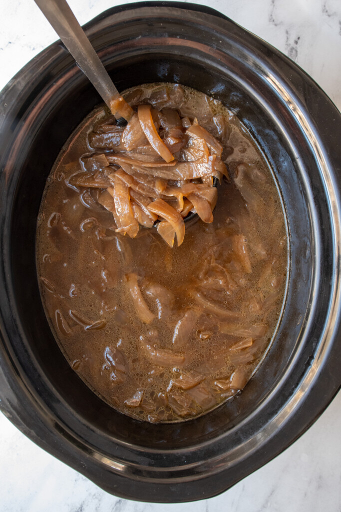 Slow cooker filled with French onion soup and a ladle showing off the soup.