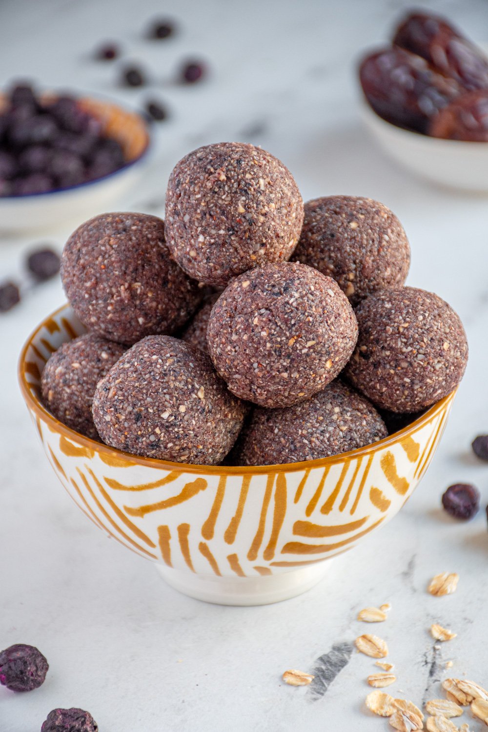 Bowl of purple colored blueberry energy balls surrounded by freeze dried blueberries.