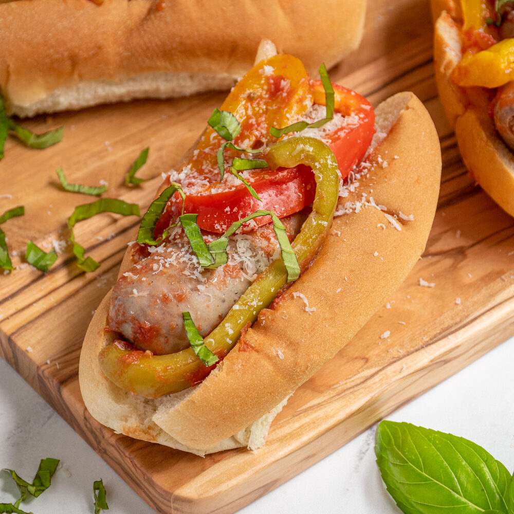 An Italian Sausage with peppers and onions in a bun topped with fresh basil and grated parmesan cheese.