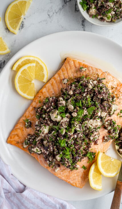 Overhead view of a white plate with a large piece of salmon topped with olive tapenade and feta cheese.