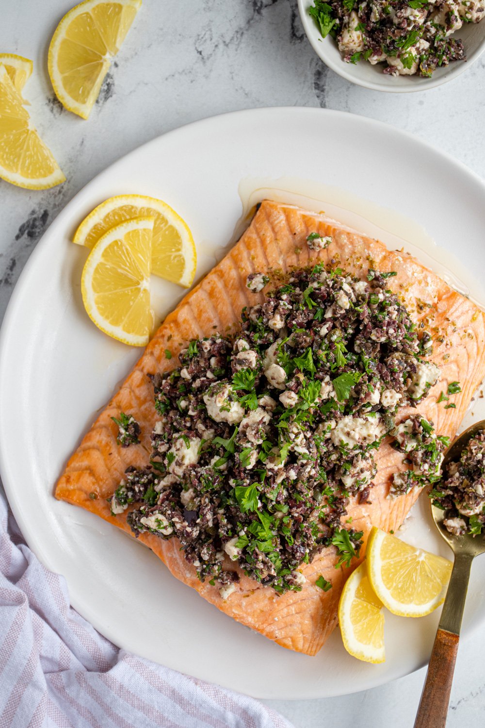 Overhead view of a white plate with a large piece of salmon topped with olive tapenade and feta cheese.