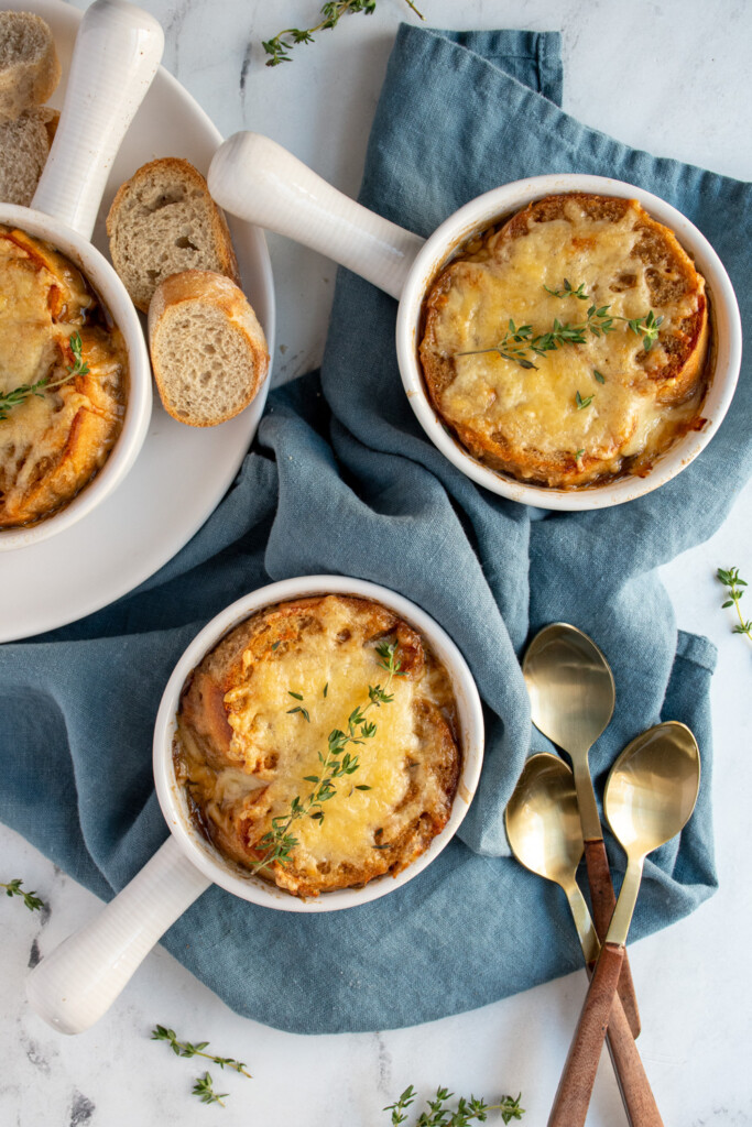 Overhead view of white bowls filled with French onion soup, topped with baguette and melted cheese for serving.