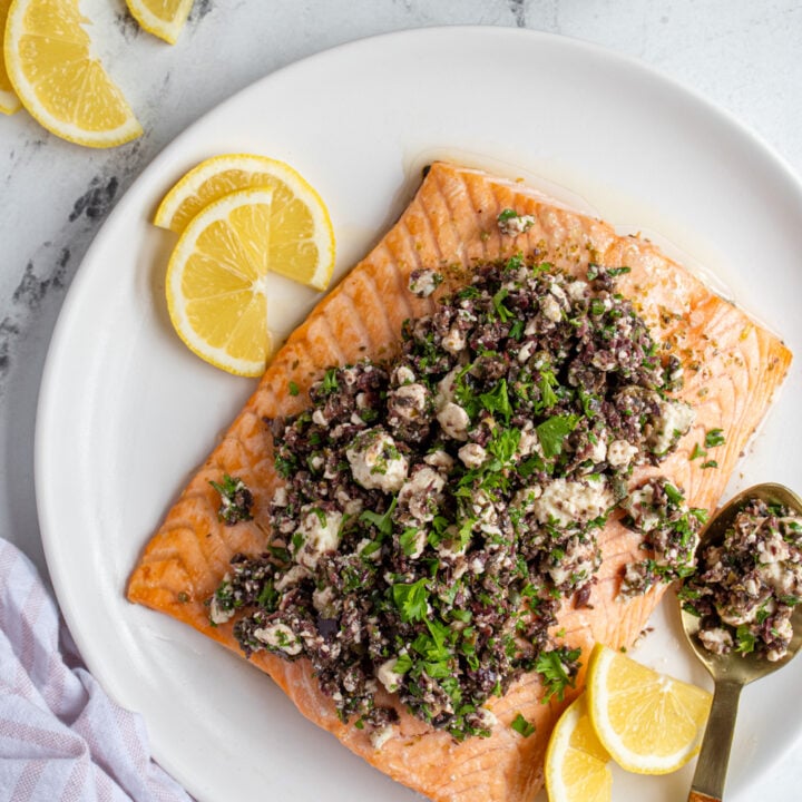 Overhead view of a white plate with a large cooked fillet of salmon topped with olive tapenade.