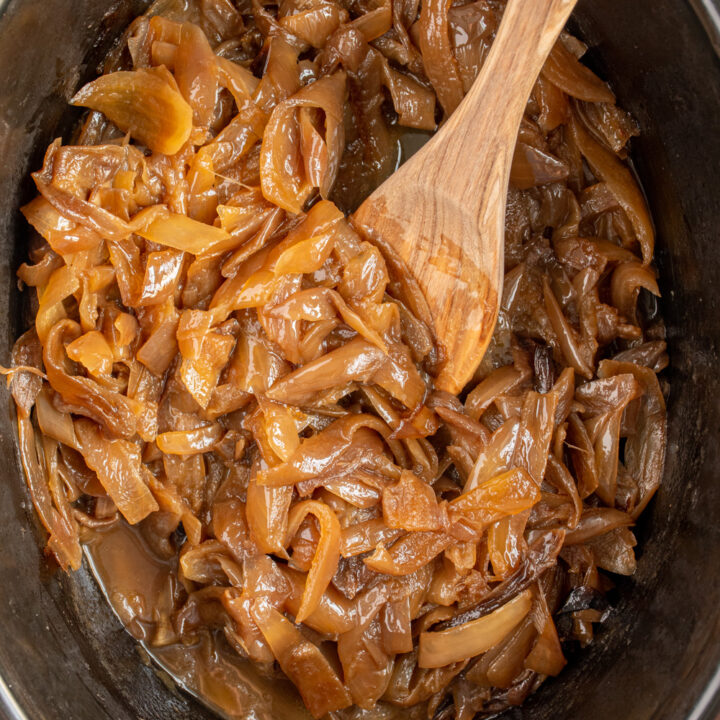 Slow Cooker Caramelized Onions in a black crockpot with a wooden spoon.